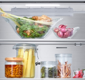 Vista de cerca del estante inferior del congelador del frigorífico LG con alimentos varios en recipientes de cristal.