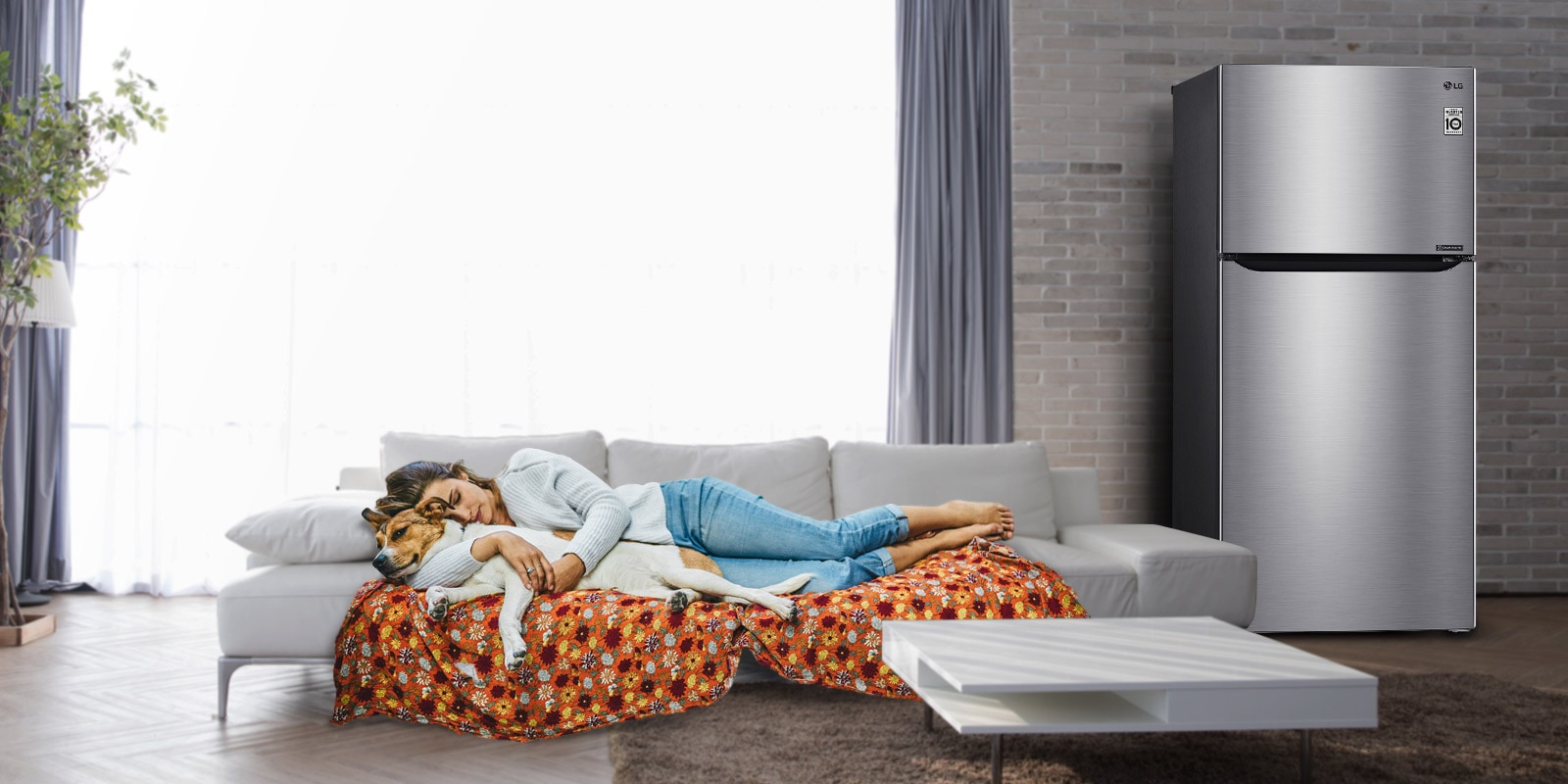 Una mujer y un perro duermen en un sofá cerca de la nevera.