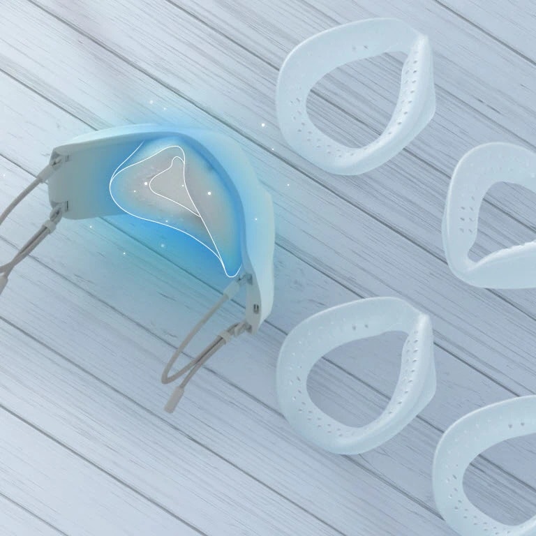 Se muestra la parte interior de la mascarilla vista desde arriba, mostranto la cubierta interior y las piezas del protector de silicona alrededor, todo sobre una mesa. Se ha resaltado de color azul la zona donde debe ir el protector facial.  