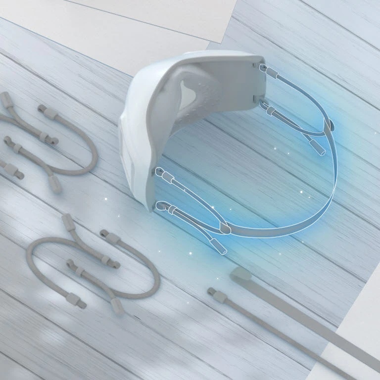 Se muestra la parte superior e interior de la mascarilla vista desde arriba, resaltando en color azul las bandas elasticas sujetas. Las bandas extra-elásticas aparecen alrededor de la mascarilla sobre la mesa.