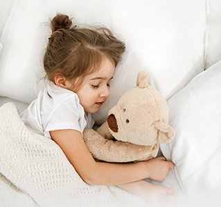 Una niña está acostada en la cama con un peluche en los brazos.