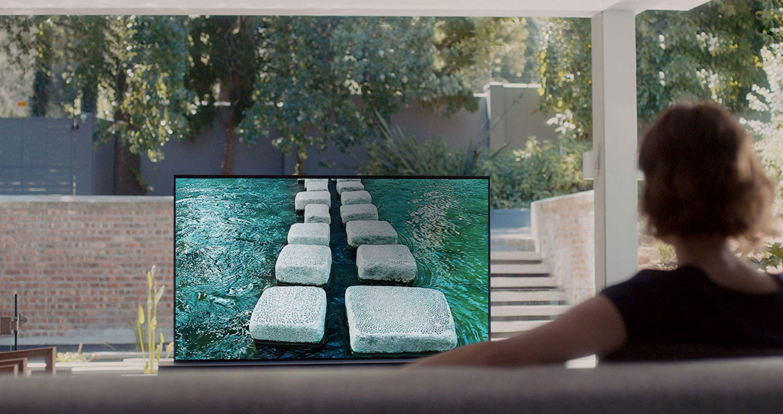 Mujer mirando un televisor que muestra un puente de piedra en una casa lujosa (reproducir el video)
