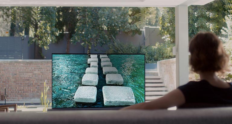Mujer mirando un televisor que muestra un puente de piedra en una casa lujosa (reproducir el video)