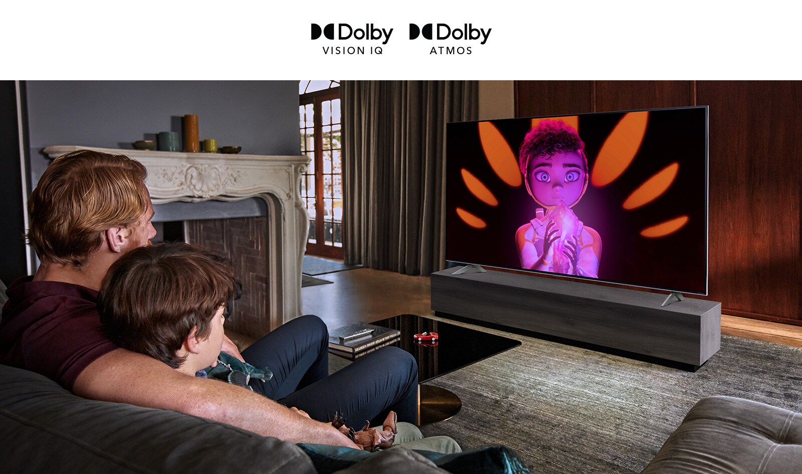 Un hombre y un niño sentados uno junto al otro en un sofá mirando una película en un televisor de pantalla plana grande. La pantalla muestra un personaje animado sobre un fondo negro.
