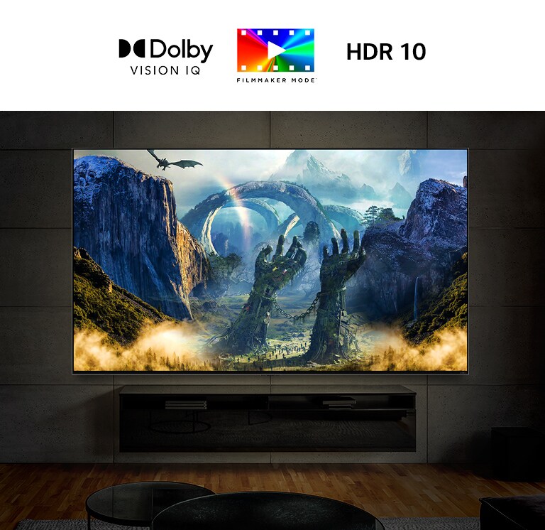 Un televisor ultra grande montado en una pared en una habitación oscura. La pantalla muestra una escena de fantasía con un dragón respirando fuego hacia el suelo.