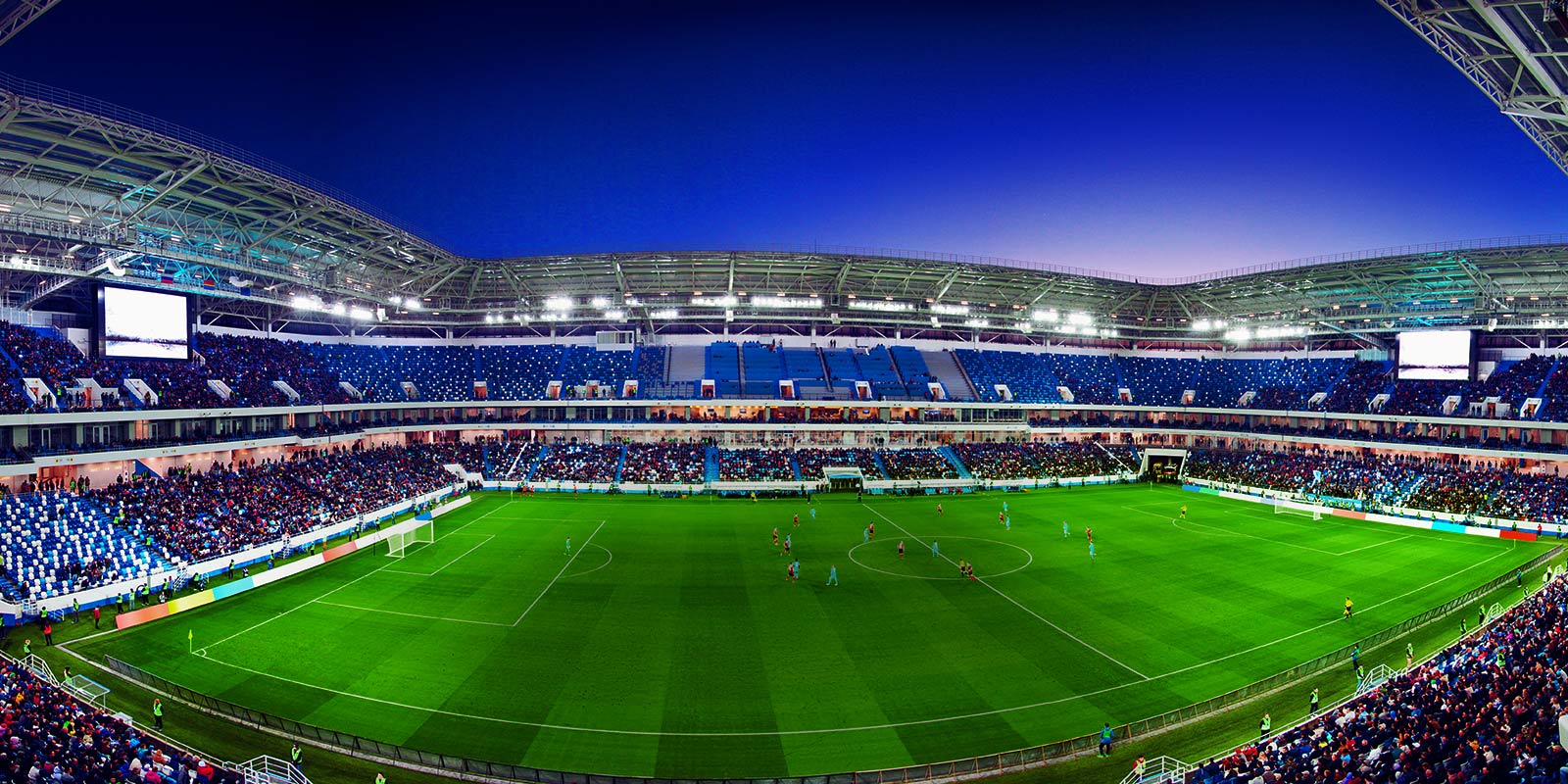 Una toma panorámica de un estadio de fútbol lleno de público y con el partido en progreso.