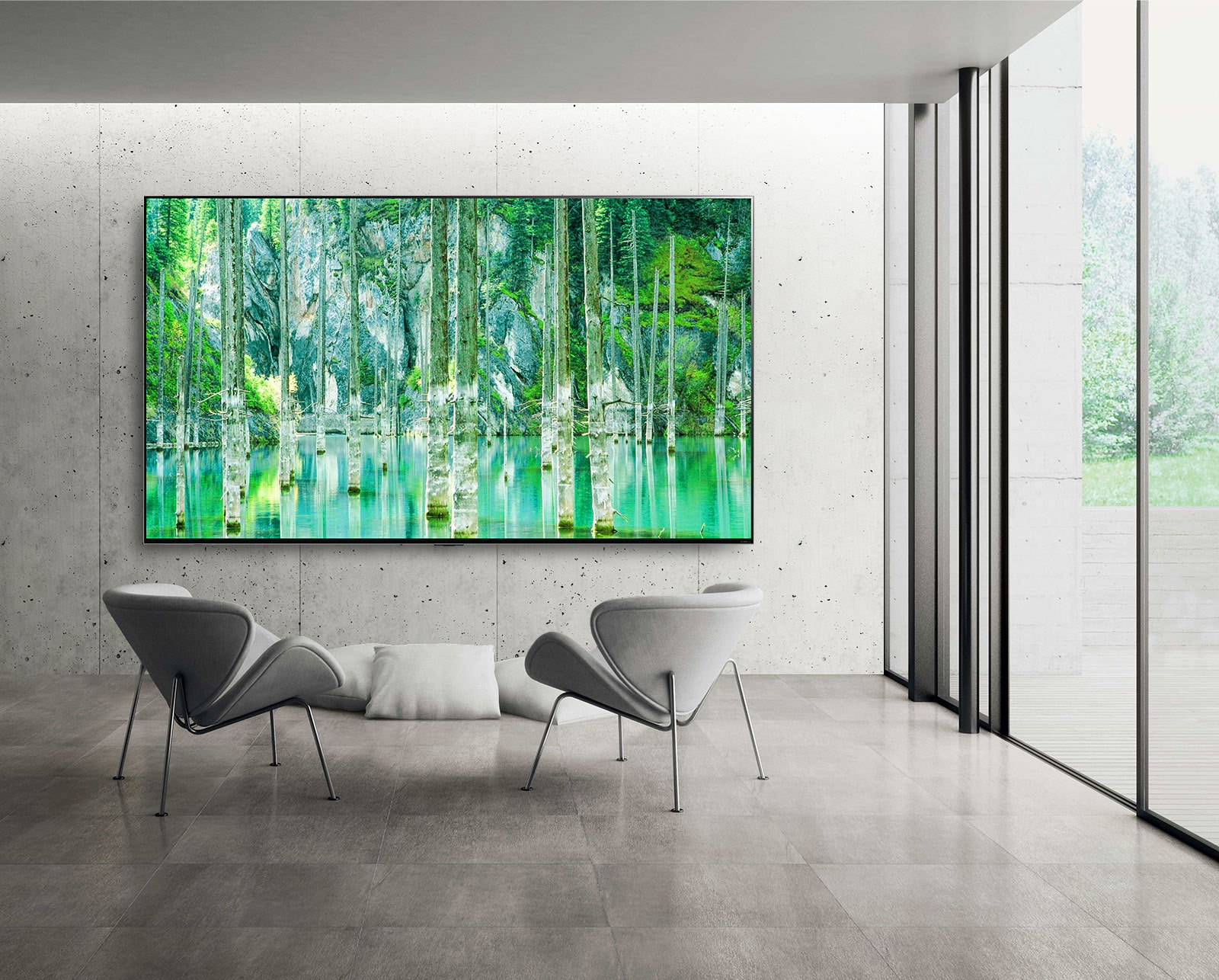 Una imagen de un televisor LG QNED MiniLED de pantalla grande montado en una pared gris de cemento sin detalles decorativos. Hay dos sillas dispuestas frente al televisor y en la pantalla se ve una escena natural de color verde.