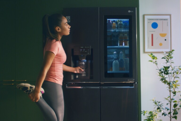 Mujer bebiendo agua filtrada del dispensador de agua del refrigerador después de hacer ejercicio