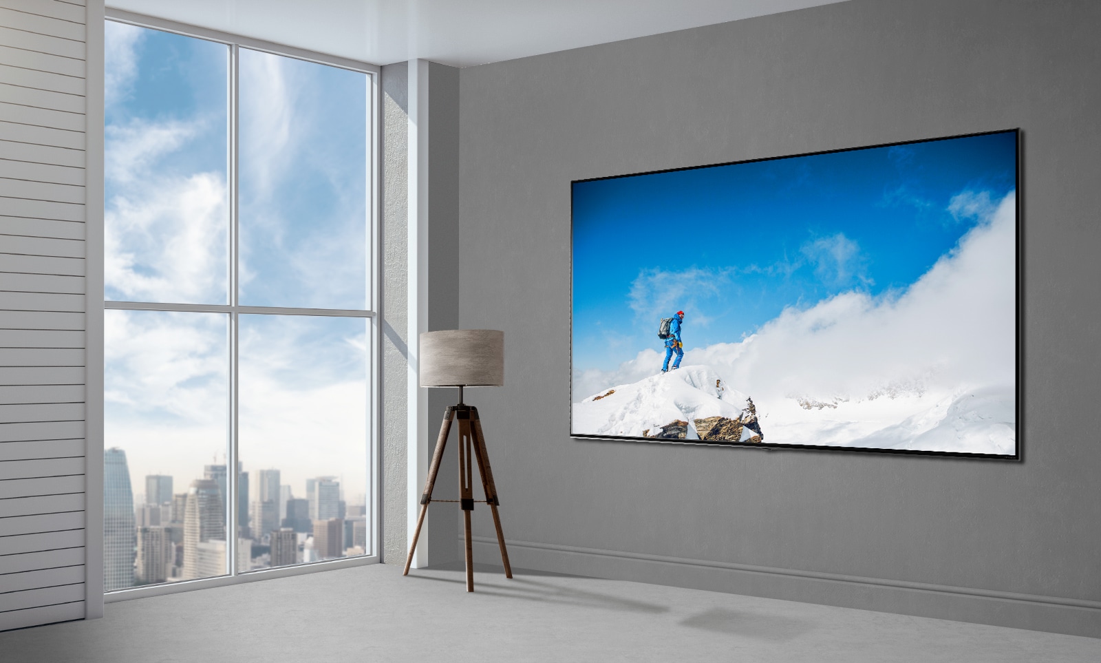 La imagen de un televisor de pantalla plana montado en una pared gris junto a una ventana que va del suelo al techo muestra un paisaje urbano. Hay una lámpara a la izquierda del televisor y la pantalla muestra a un excursionista en una roca cubierta de nieve con un cielo azul y nubes de fondo.
