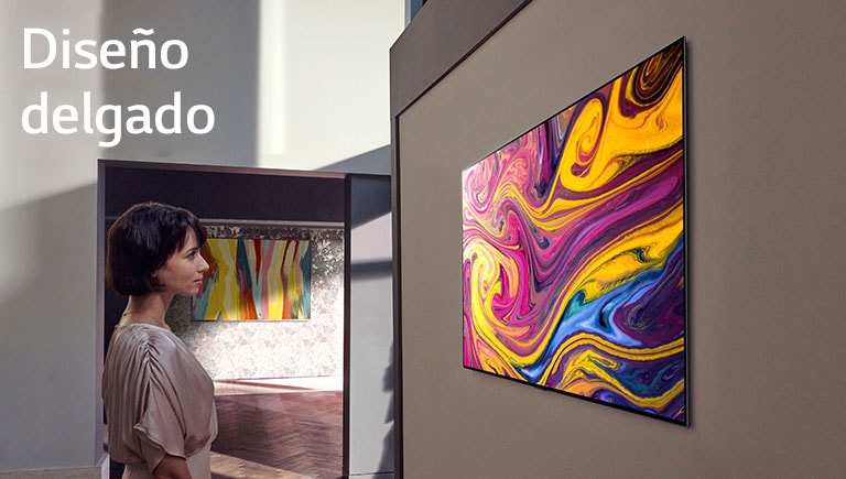 Una mujer está mirando un televisor colgado en la pared en el que se muestra una obra de arte.