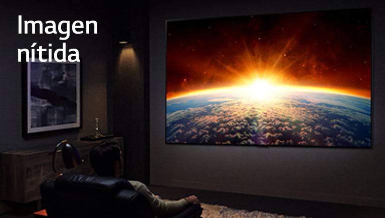 Un hombre, sentado en el sofá de una habitación oscura, está viendo en el televisor cómo el sol sale por detrás de la tierra.