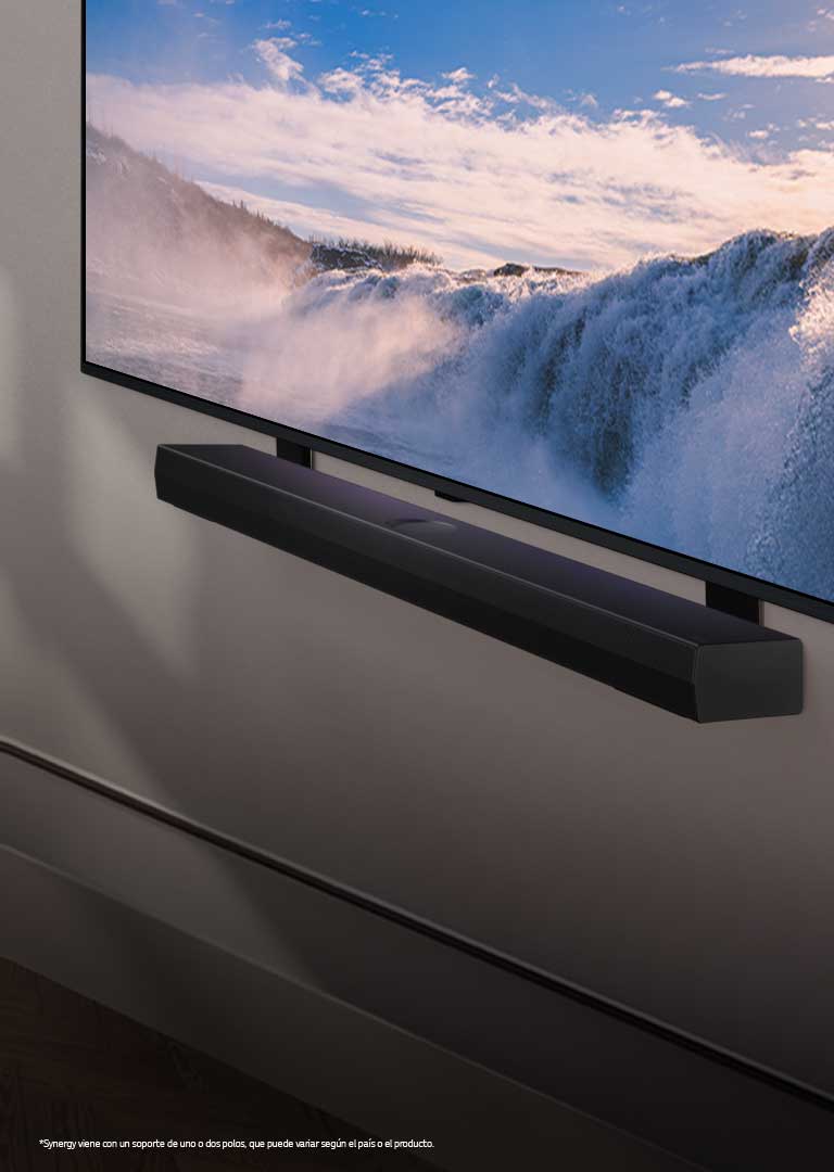 LG TV y Soundbar colocados en una perspectiva en ángulo montados en una pared. En la TV, se muestra un primer plano de una gran cascada y la luz suave del sol cae sobre la pared, la TV y la barra de sonido. Un aviso legal que dice lo siguiente: “Synergy viene con un soporte de uno o dos polos, que puede variar según el país o el producto”.