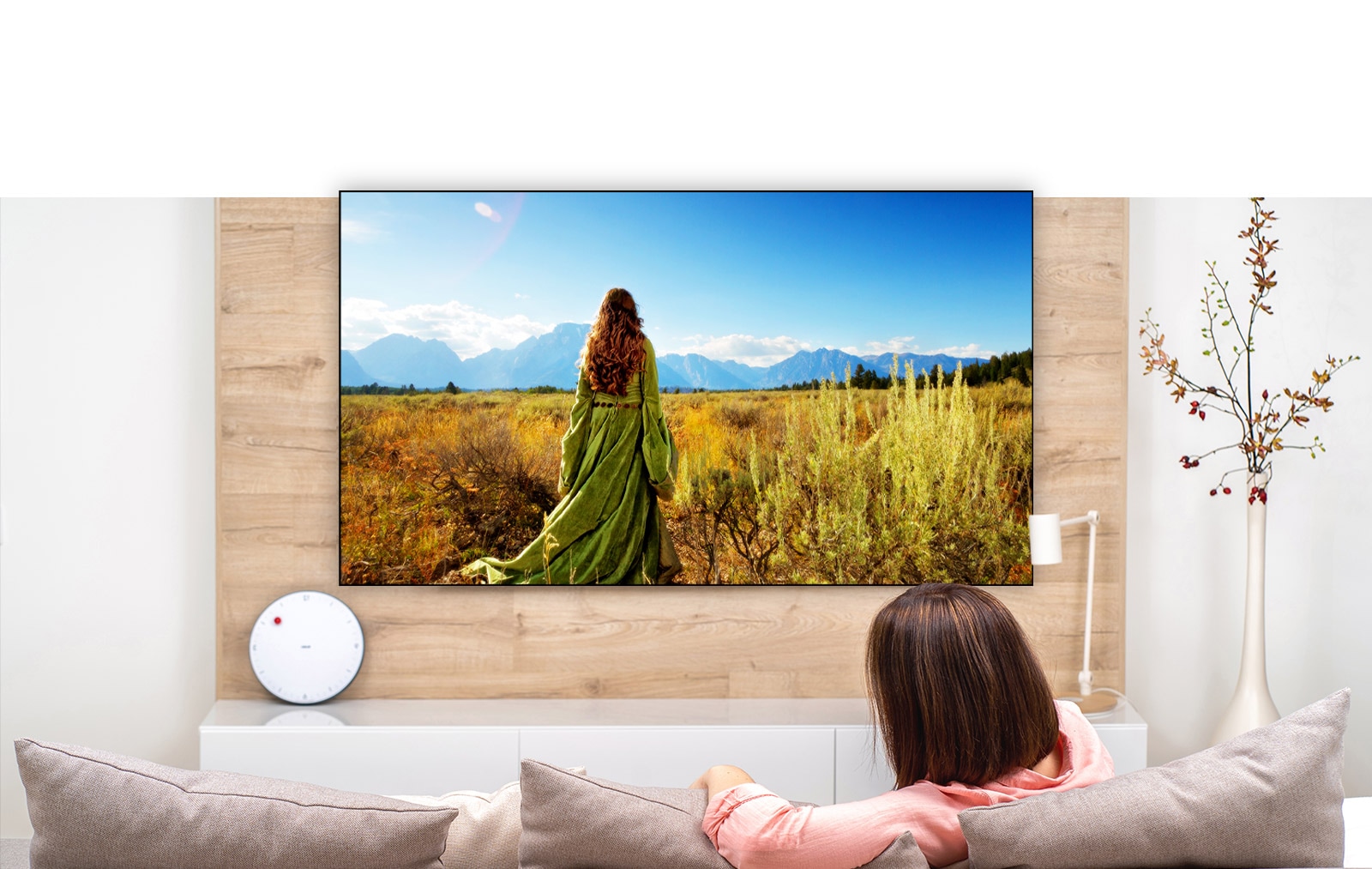 Una pantalla de televisión que muestra una escena de una película de fantasía con una mujer de pie en los campos mirando hacia a las montañas.