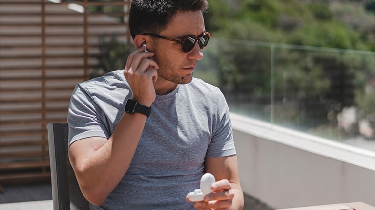Imagen de un hombre con gafas de sol quitando uno de los auriculares LG TONE Free