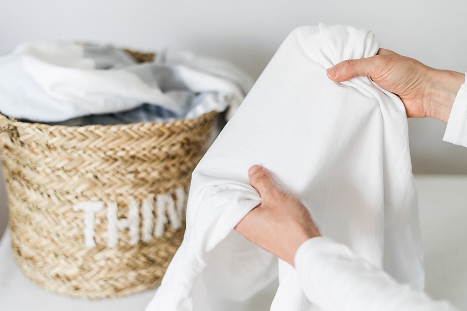 Frisch gewaschene weiße Kleidung, mit einem Wäschekorb voller Kleidung im Hintergrund