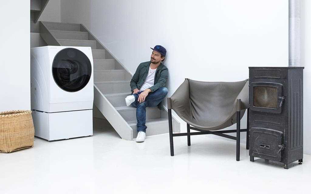A man who sits on the stairs next to his LG TWINWash washing machine with various artistic furniture around him