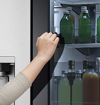 The front view of a black glass InstaView refrigerator with the light on inside. Hands knocking on InstaView screen.