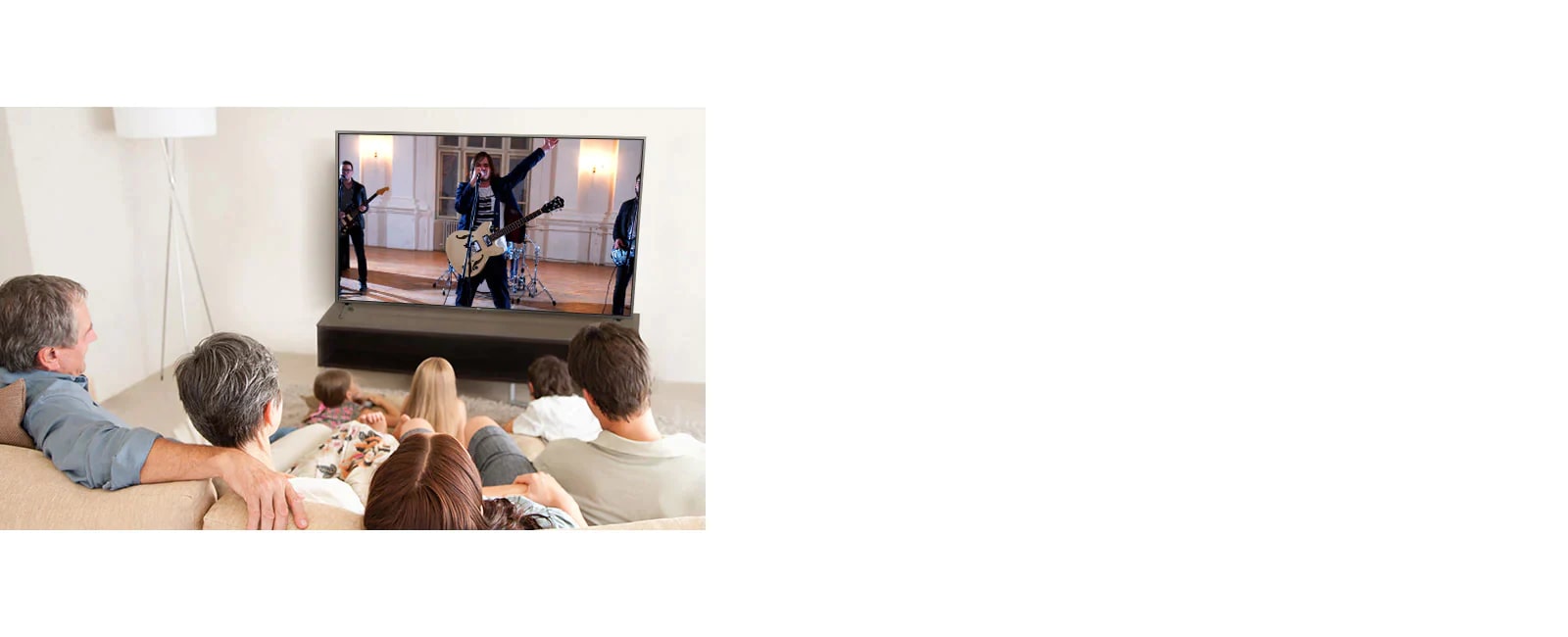 Family of seven gathered in the living room, watching a movie. TV screen shows a band performing.