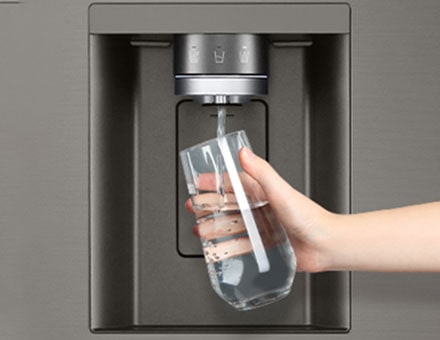 A person is getting water from the refrigerator dispenser in a cup