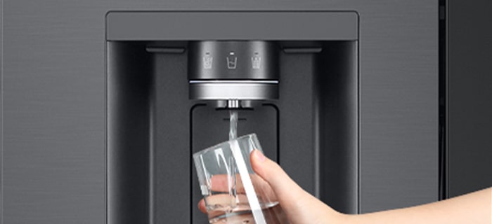 A person is getting water from the refrigerator dispenser in a cup