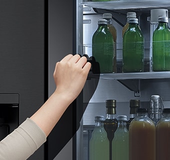 The front view of a black glass InstaView refrigerator with the light on inside. Hands knocking on InstaView screen.