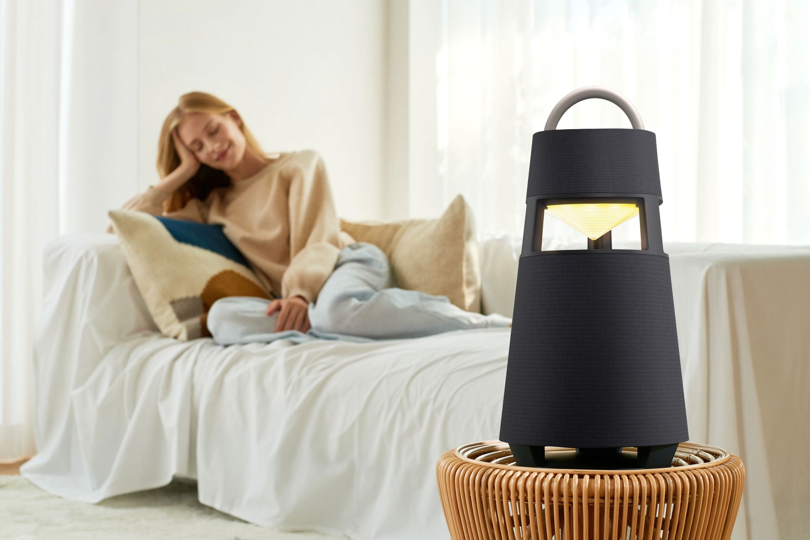 An image of a woman sitting on a sofa listening to music with an XBOOM 360 in front of her.