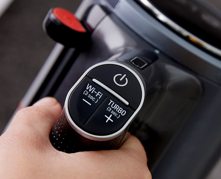 A hand is gripping the handle of the handstick vacuum cleaner. The handle shows the on/off button, Wi-Fi button and Turbo button.