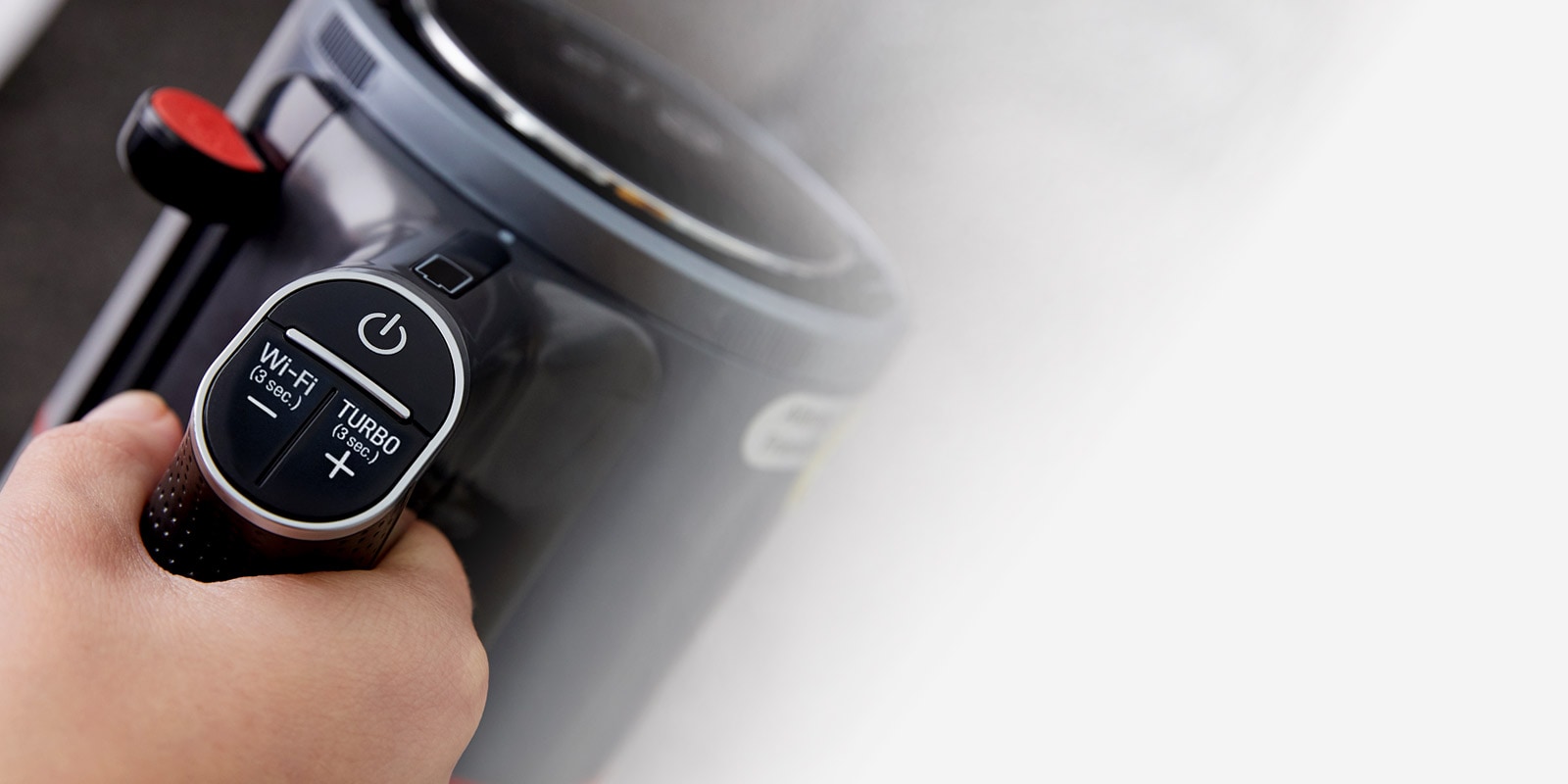 A hand is gripping the handle of the handstick vacuum cleaner. The handle shows the on/off button, Wi-Fi button and Turbo button.