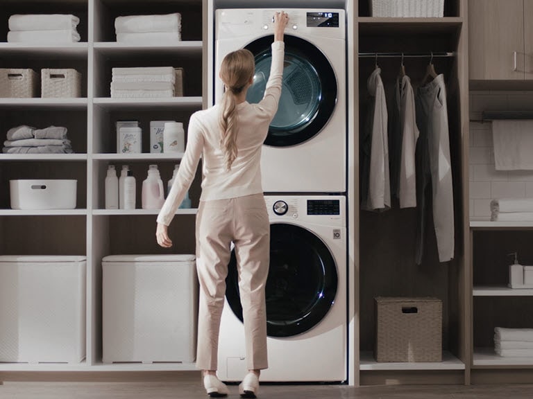 The first image is a combination of two images, one a older style white washer and dryer stacked on top of each other and installed in a wall unit and one a white LG Wash Tower installed in a wall unit. A dotted line and a red circle icon at the center with arrows indicates you can move from left to right to see each image in its entirety.