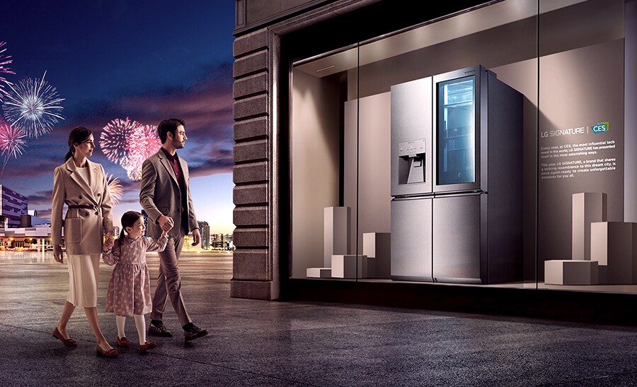 A family of three observes the LG SIGNATURE Refrigerator on display at the CES gallery, while fireworks set off behind them.