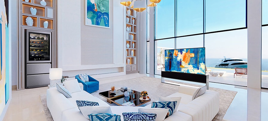 LG SIGNATURE Rollable OLED TV R and Wine Cellar in a white-and-blue-themed room in front of large windows with a view of the ocean.