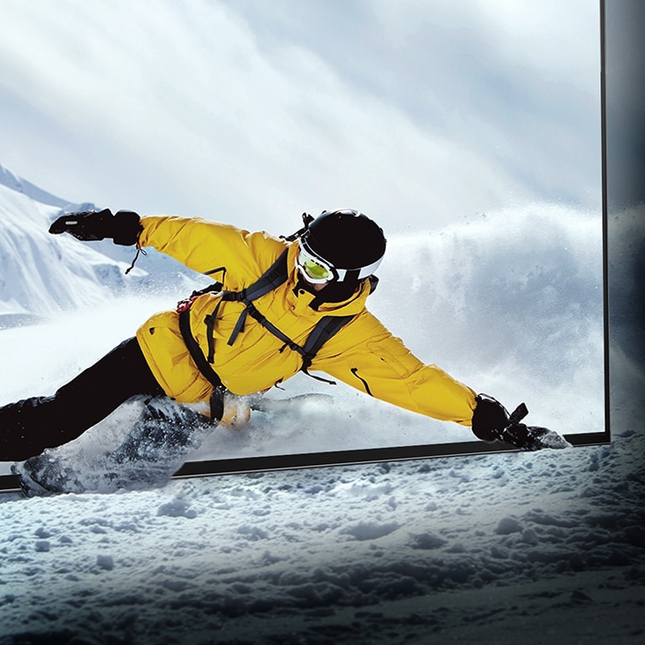 A snowboarder leaning through the screen of the LG OLED television while the snow comes to life in the room.