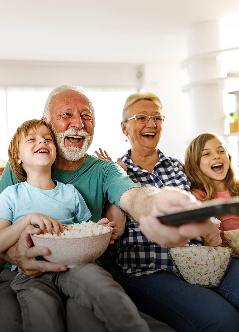 A family sits laughing while the grandfather points the remote outward.