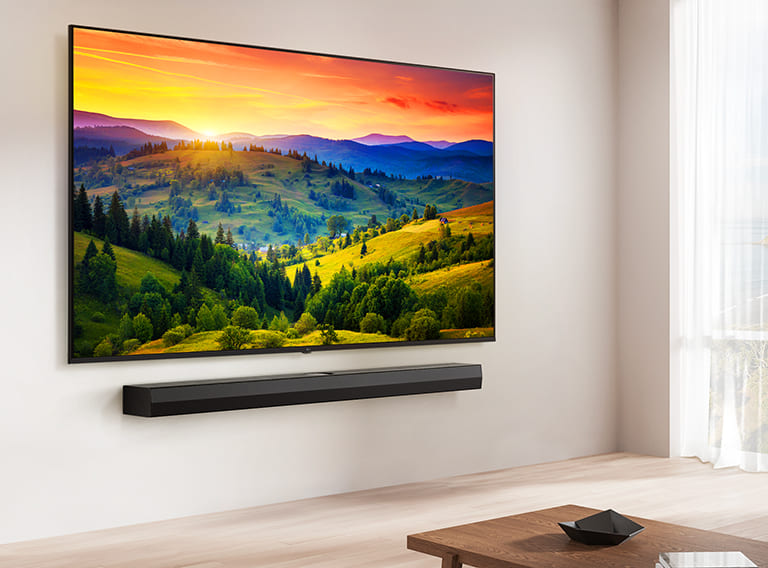 LG UHD TV mounted on a wall above a LG Soundbar in a modern living room space. LG UHD TV depicts a colorful background.
