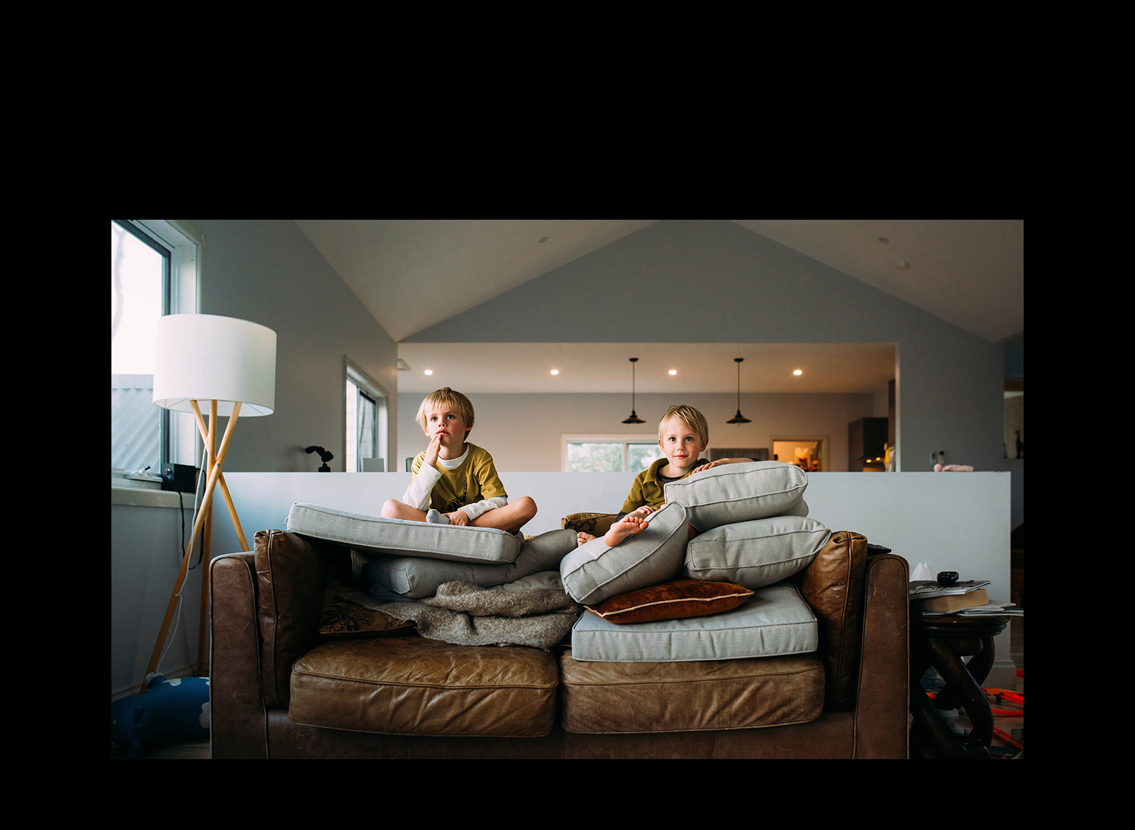 Two twin boys are watching something sitting on a sofa.