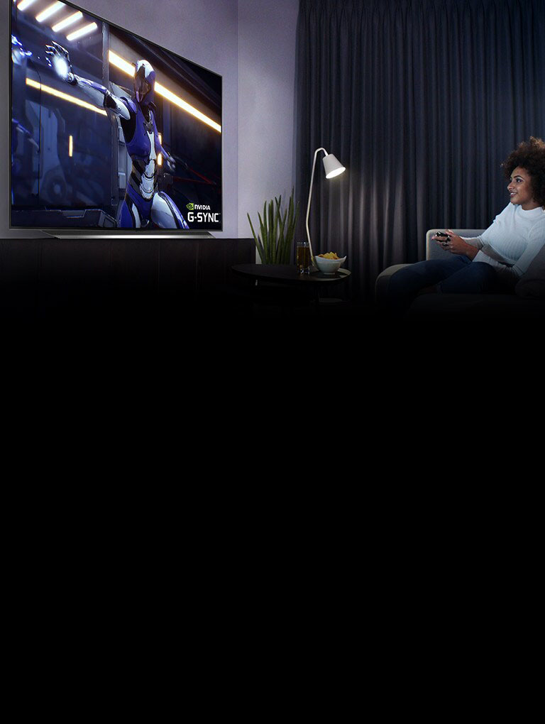 Woman sitting on a sofa, holding a joystick while playing a game on a TV screen