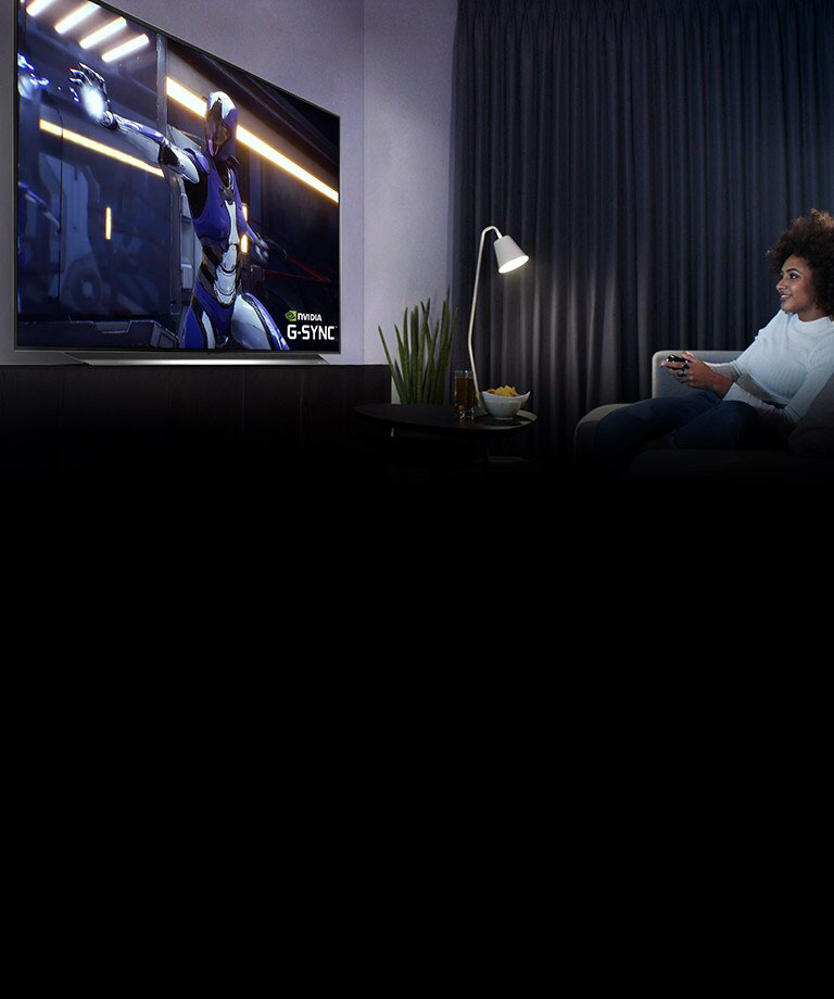 Woman sitting on a sofa, holding a joystick while playing a game on a TV screen