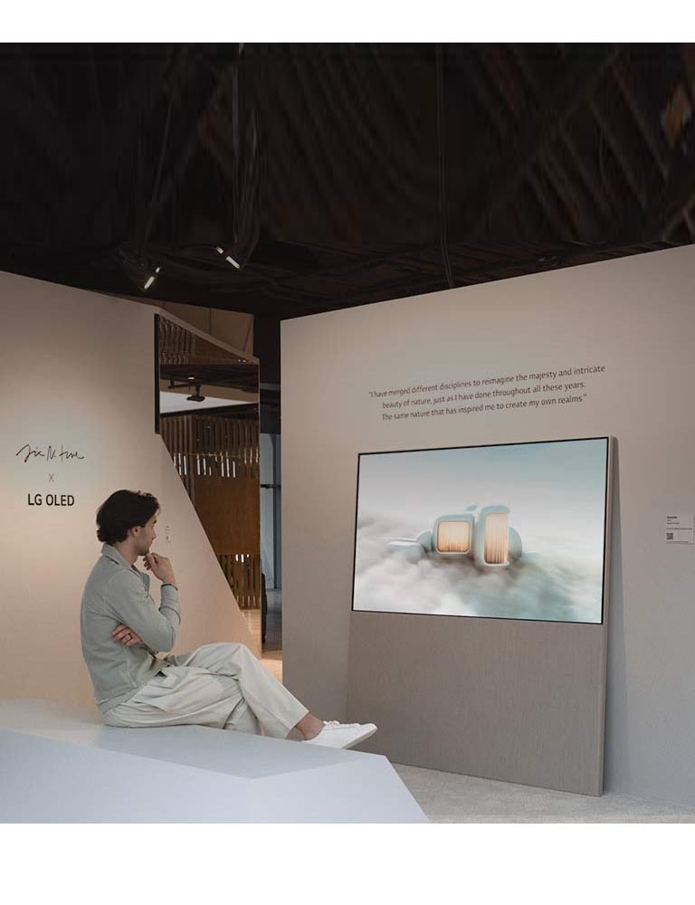 L’image montre une personne assise sur une chaise qui regarde un paysage onirique au milieu des nuages sur l’Easel. Sur un autre mur, un écran LG OLED montre une image d’arbres enneigés s’élevant vers le ciel.