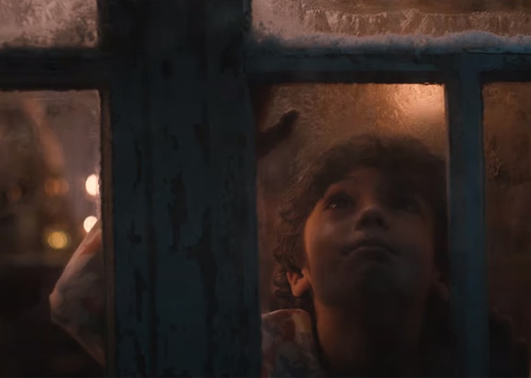 Un enfant regarde dehors par une fenêtre enneigée