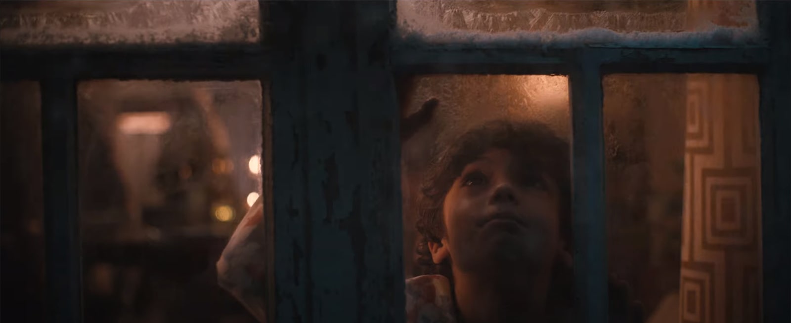 Un enfant regarde dehors par une fenêtre enneigée