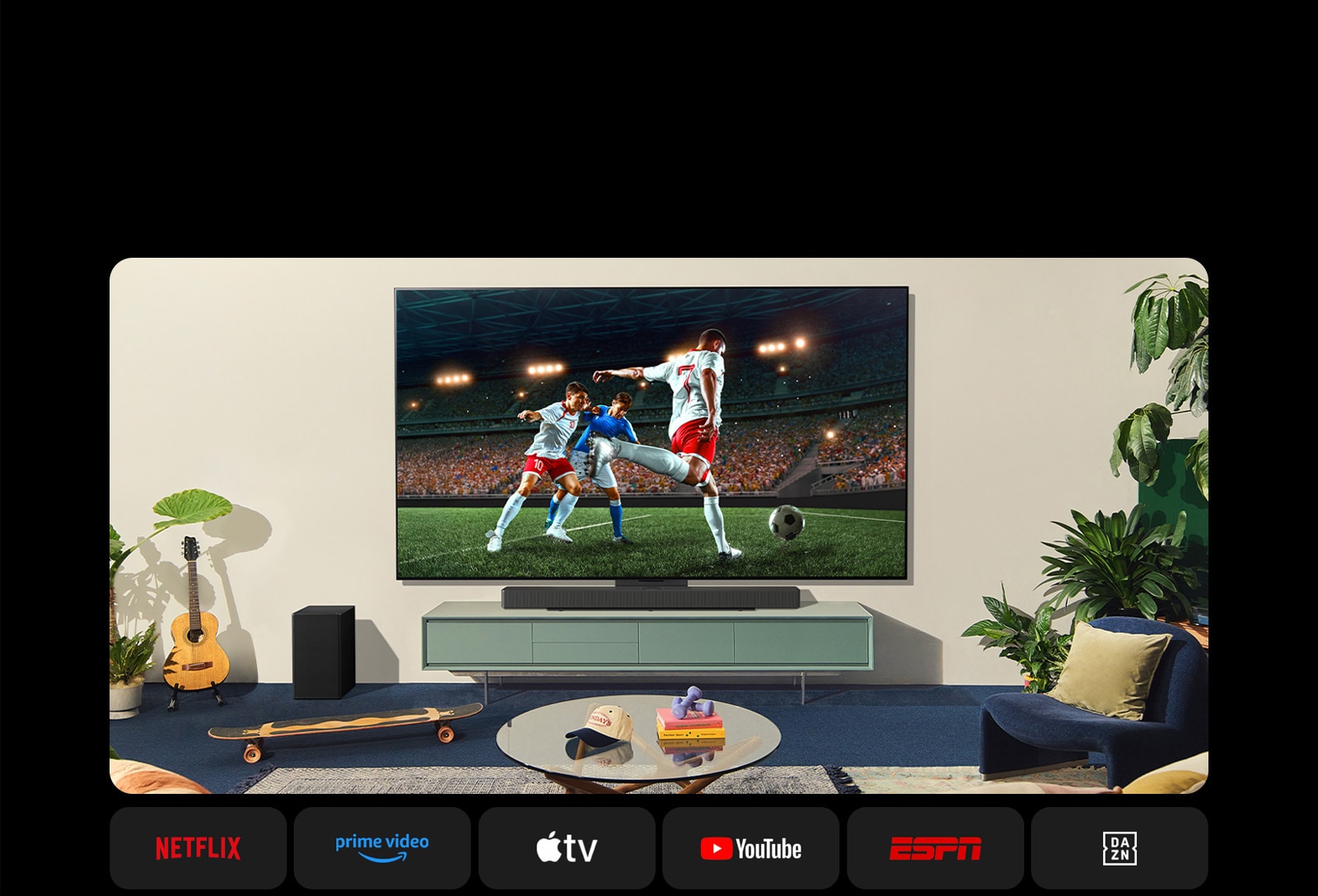 Deux femmes regardent un match de football dans un espace confortable. Une femme tient à ballon de football et toutes deux supportent leur équipe avec des haut-parleurs jaunes et rouges. Les logos suivants sont affichés en dessous. Netflix, Amazon Prime Video, Apple TV, Youtube, ESPN et DAZN.