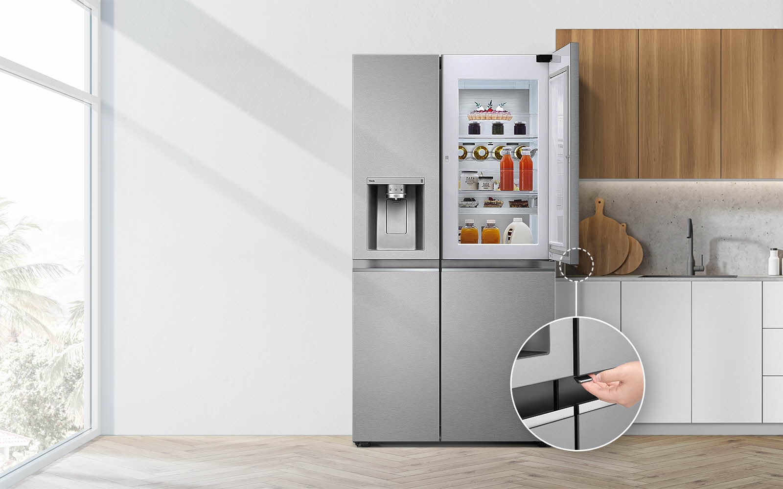 Le réfrigérateur est présenté de face, installé dans une cuisine. La porte supérieure droite est ouverte et un cercle et une ligne mènent vers un cercle de plus grande taille, qui présente un zoom sur le bouton dans le coin inférieur droit de la porte ouverte, qui est dotée d’un bouton d’ouverture caché.