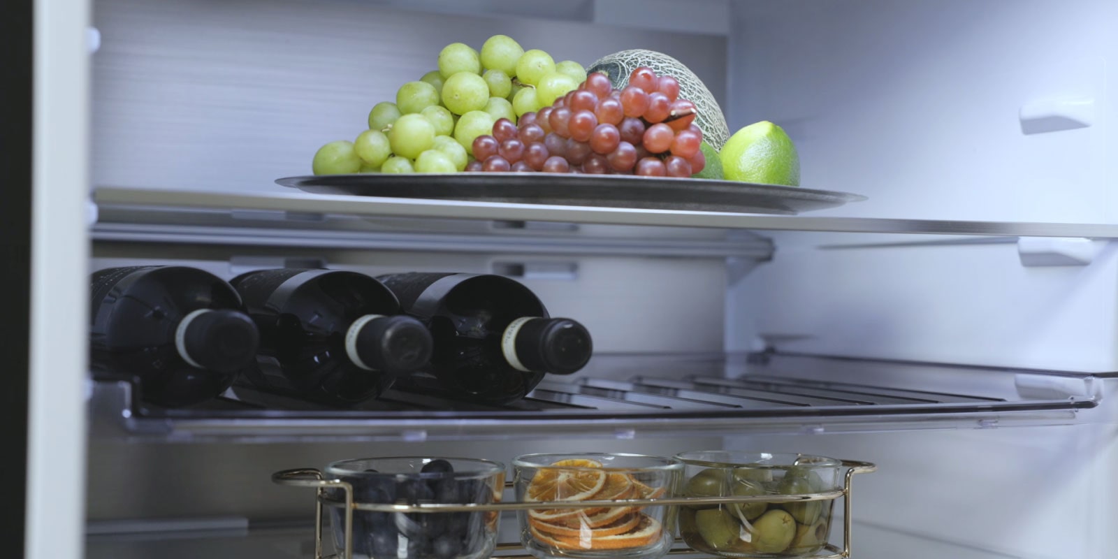 Vue intérieure du réfrigérateur congélateur LG (GBBW322CEV) avec des fruits sur l'étagère supérieure, des bouteilles de vin au milieu et d'autres fruits sur l'étagère inférieure.	