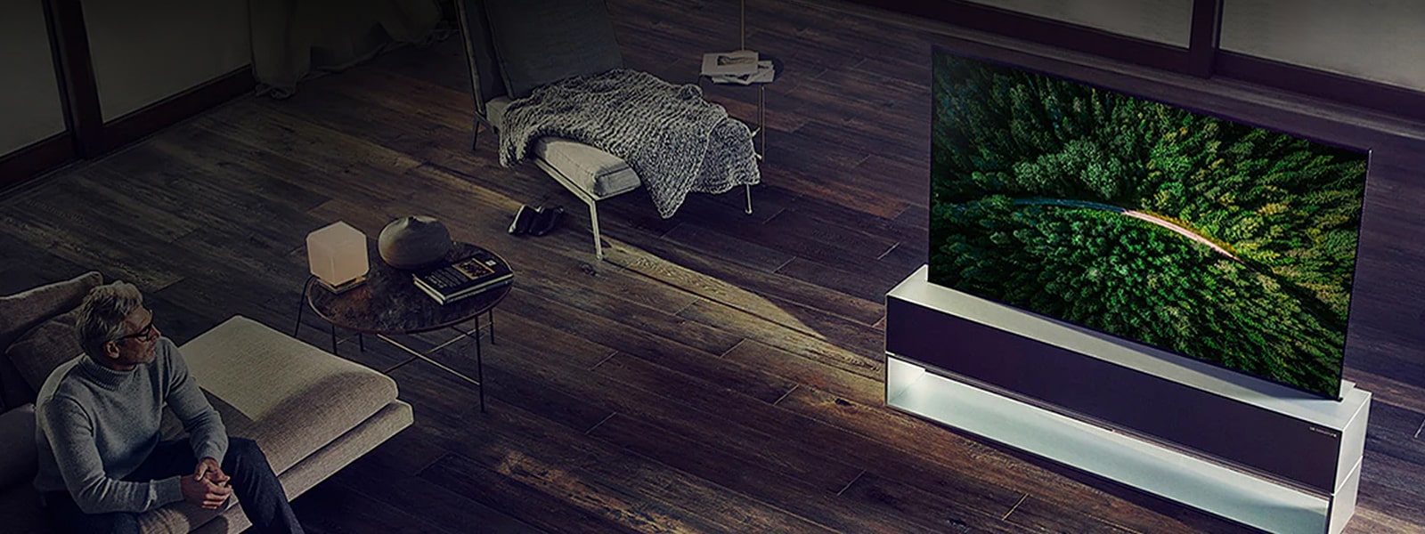 Le téléviseur OLED enroulable LG SIGNATURE est placé sur le parquet du salon de luxe et un homme regarde la télévision.
