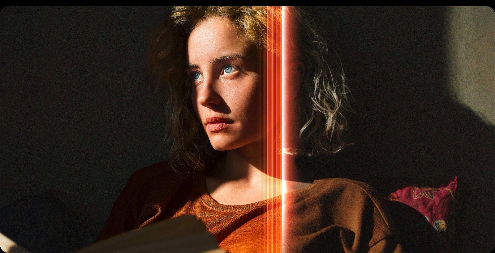 Une femme avec des yeux bleus perçants et un top orange brûlé dans un espace sombre. Des lignes rouges représentant les ajustements IA couvrent une partie de son visage qui est clair et riche en détail, tandis que le reste de l’image semble terne. 