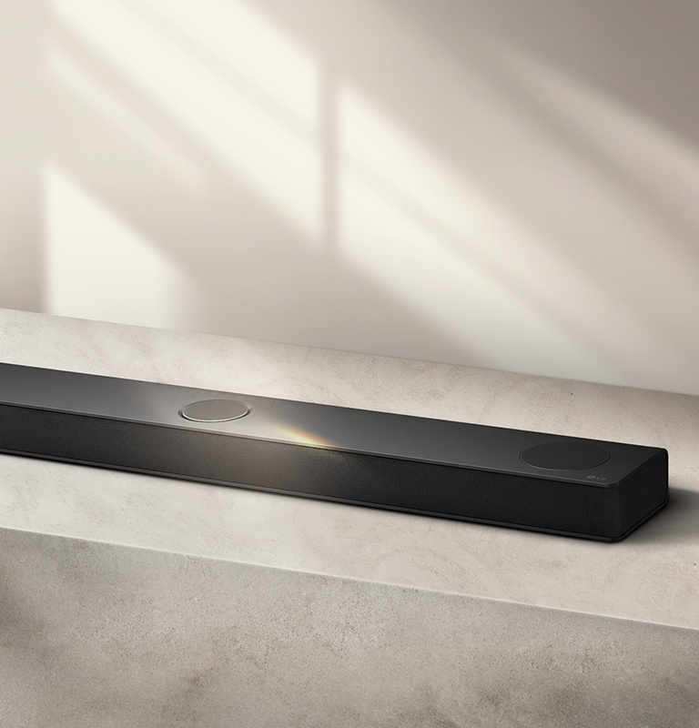 Vue aérienne inclinée d’une LG Soundbar sur une surface grise contre un fond gris.