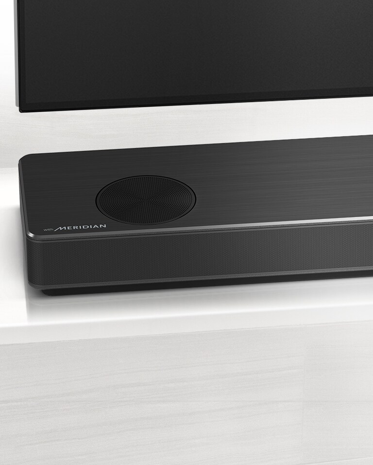 Gros plan de la barre de son LG sur le côté gauche, avec le logo Meridian en bas à gauche. Le côté inférieur gauche du téléviseur est également visible. 