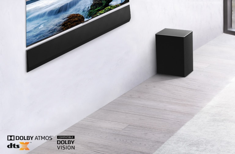 Le téléviseur et la barre de son LG sont fixés au mur avec un caisson de graves en dessous et à droite. Le téléviseur présente un coucher de soleil en mer.