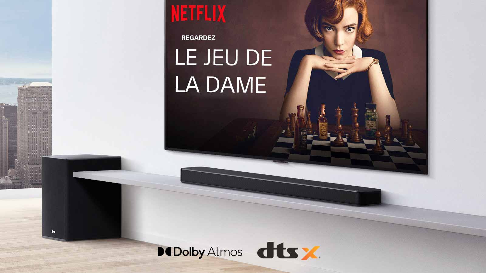 Le téléviseur est fixé au mur. Une affiche d’une émission de télévision est diffusée sur l’écran du téléviseur. La barre de son LG se trouve juste en dessous du téléviseur sur une étagère blanche avec un caisson de basses juste à côté. Logos Dolby Atmos et DTS: X affichés au milieu en bas de l’image.