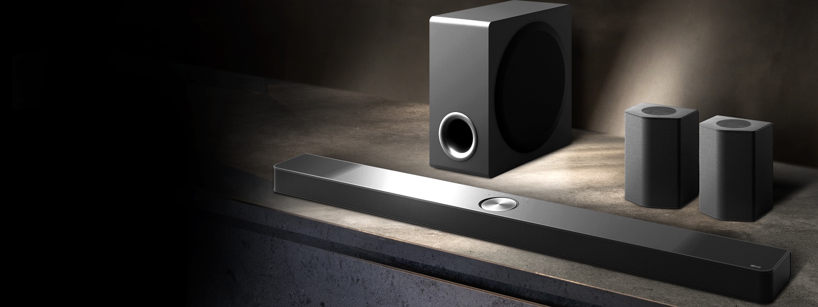 LG Soundbar, enceintes arrière et caisson de basse installés en biais sur une étagère en bois marron dans une pièce sombre, avec une lumière qui n’éclaire que le système audio.